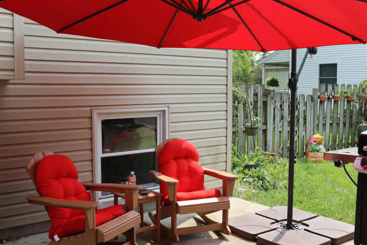 a large red umbrella hangs over two red cushioned outdoor chairs on a back patio