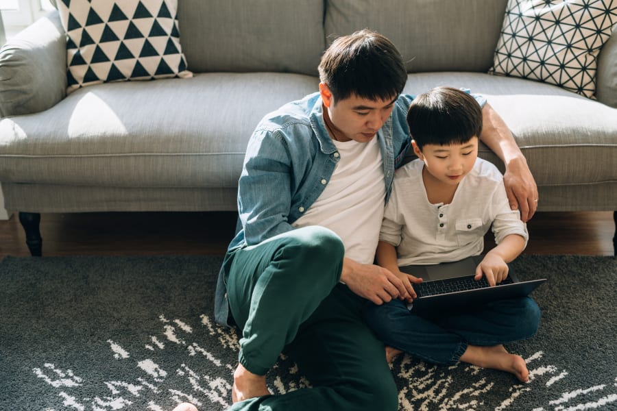 Resident student doing some homework on his laptop with help from his dad in their new home at Sofi at Forest Heights in Portland, Oregon