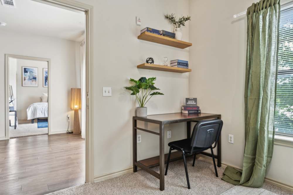 Study area with desk, plant, shelves, and green curtains; open doorway reveals bedroom with bed and wall art at Midtown 905 in Denton, Texas