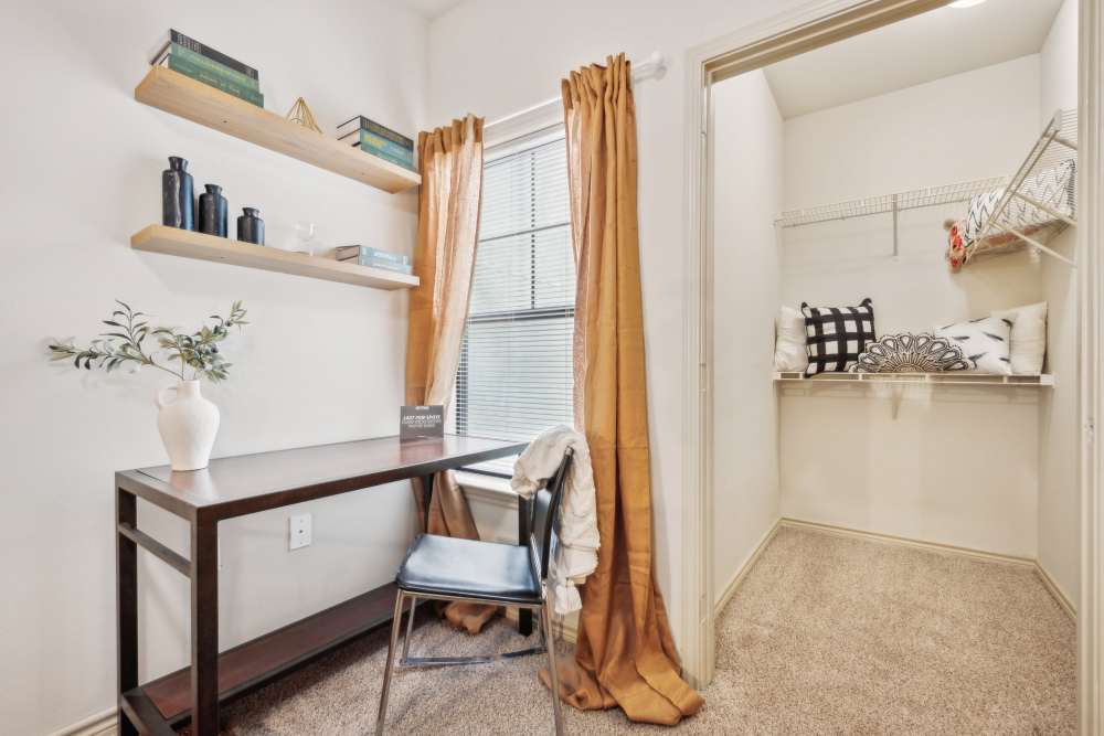 Small room with a study desk, shelves, window with brown curtains, and an open closet with storage shelves at Midtown 905 in Denton, Texas