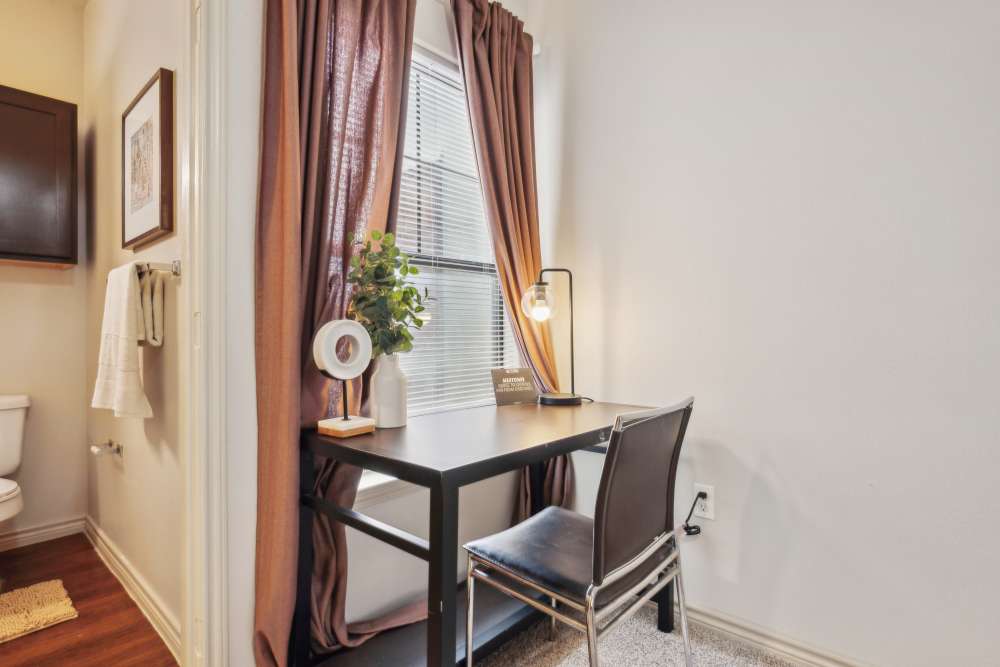 Study space with black desk, lamp, and plant by a window with brown curtains at Midtown 905 in Denton, Texas