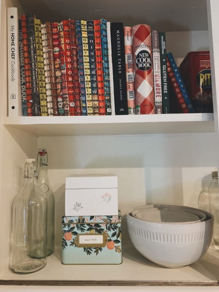 two shelves, one with books and the below shelf with dishes and a recipe box