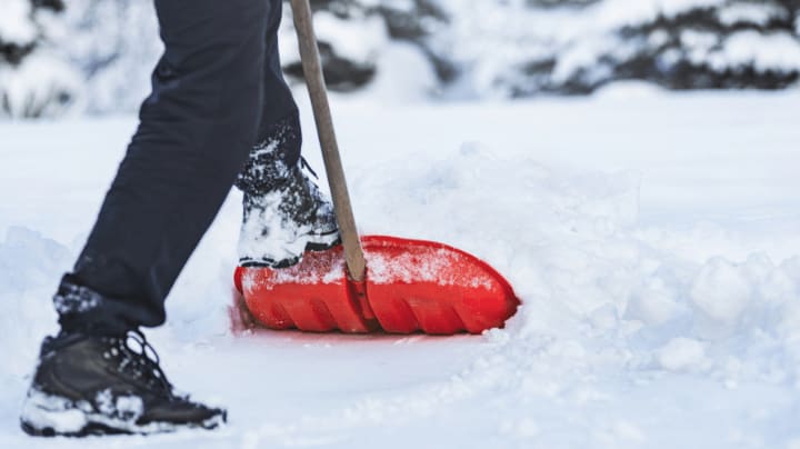 Person shoveling snow with a red shovel during winter conditions, highlighting seasonal maintenance and secure self storage solutions in Portland Oregon