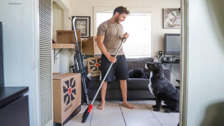 man cleaning house with broom next to dog