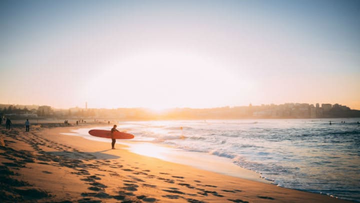 person with surfboard in distance standing on beach