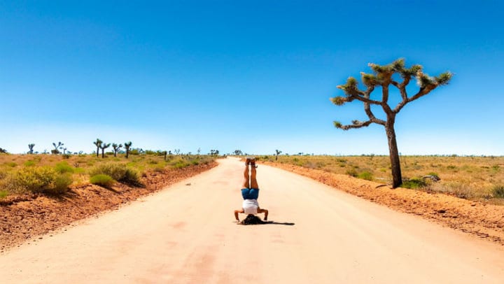 woman doing a headstand on dirt road in desert setting