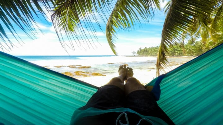 man laying on hammock looking out on beach scenery 