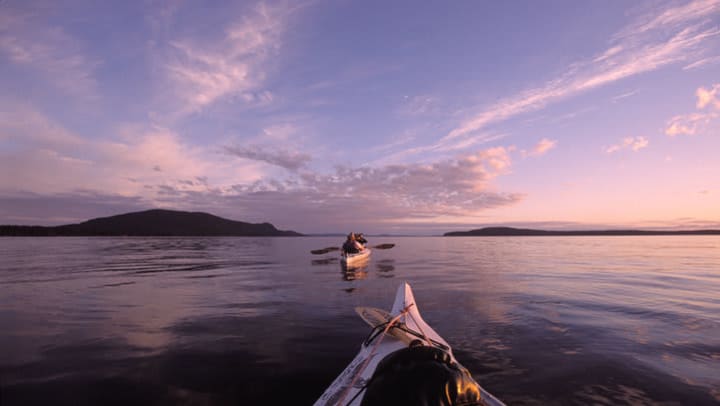 two kayaks on a large body of water heading toward islands