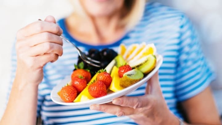 Woman holding a plate of fruit in one hand and a fork in the other hand