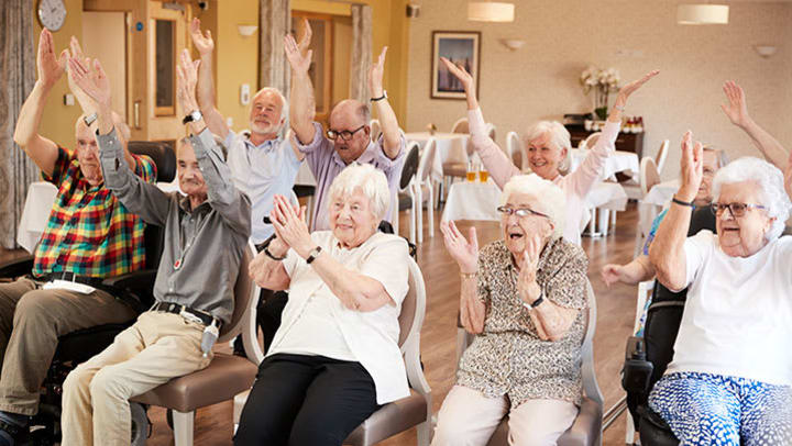 Group of seniors, seated and participating in an exercise class. 
