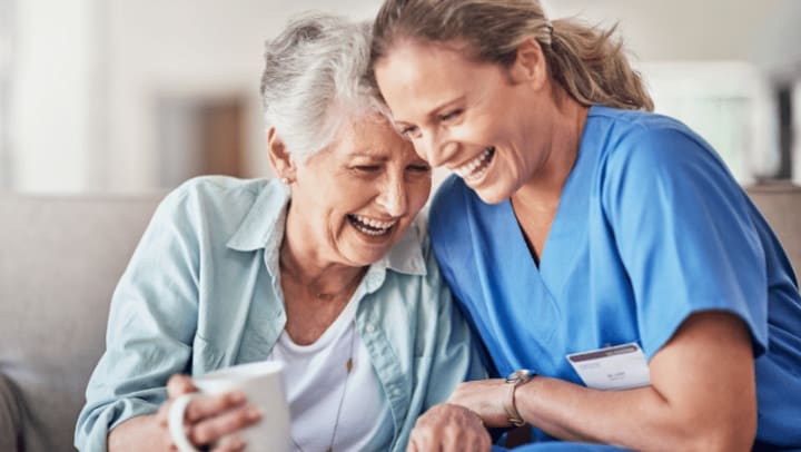 a caregiver and an old woman smiling together