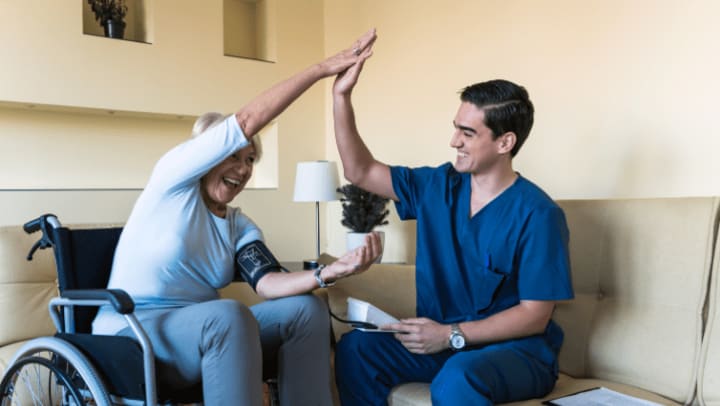 an elderly woman in a wheelchair high-fiving with her caregiver