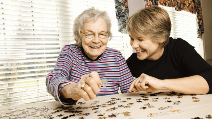 a senior lady putting together a puzzle with her leaf and looking excited. 