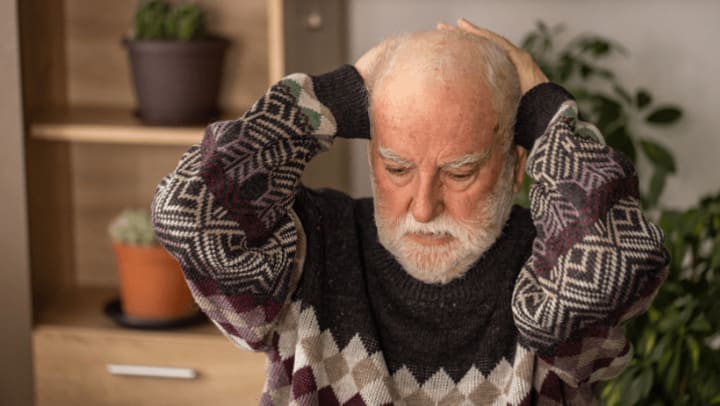 a concerned older adult holding his head in both hands 