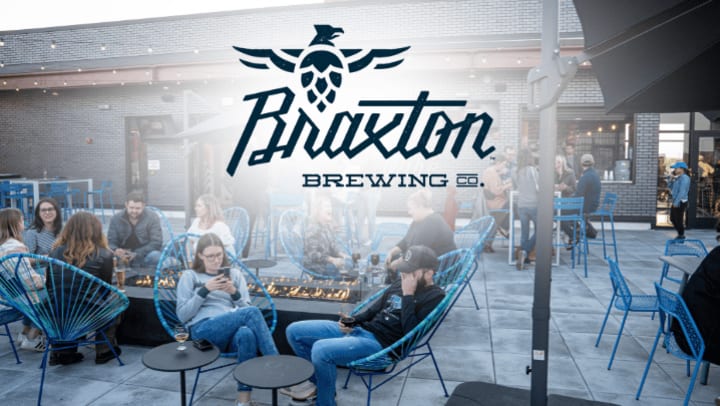 Guests relax around a firepit on a modern rooftop patio with blue chairs at Braxton Brewing Co., whose logo is prominently overlaid at the top.