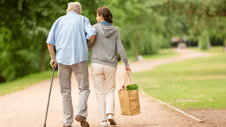 an elderly man walking with his caregiver on his arm
