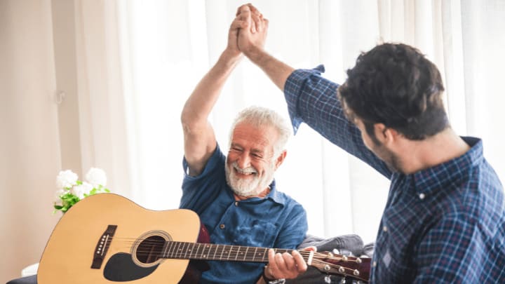 a senior man playing guitar and celebrating with his son 