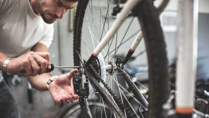Man using a tool to repair the back tire and rear chain derailleur on a bicycle near {{location_name}} in {{location_city}}, {{location_state_name}}
