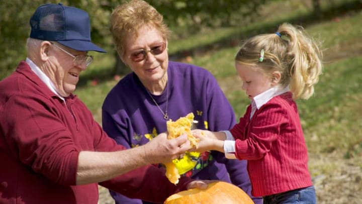 Grandparents and their grandchild carving pumpkins together outside