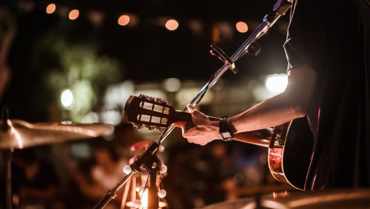 A view from behind of a singer holding an acoustic guitar and facing a crowd | live music around Destin