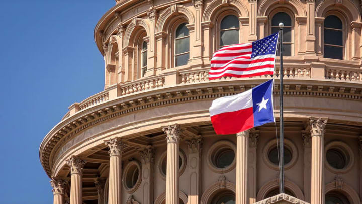 American and Texas state flags flying on the dome of the Texas State Capitol building in Austin.