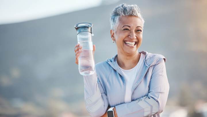 Happy senior woman drinking water on her walk outside