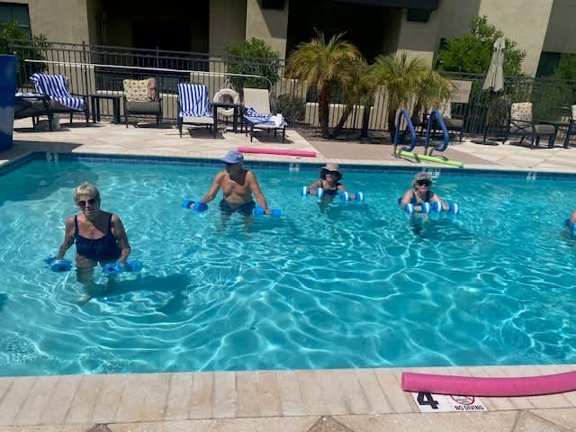 Group of senior residents participating in a pool-based fitness class on a sunny day, using foam dumbbells for low-impact resistance exercises at Clearwater Pinnacle Peak.