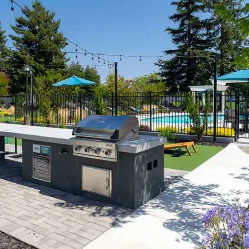 Two-BR Apartments In Rohnert Park, CA - The Lenox - BBQ Cooking Area With A View Of The Pool, Strung Light, And Cornhole Game.