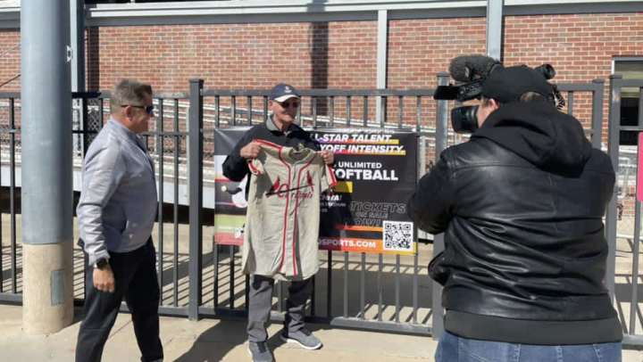 Man holding a baseball jersey while being interviewed