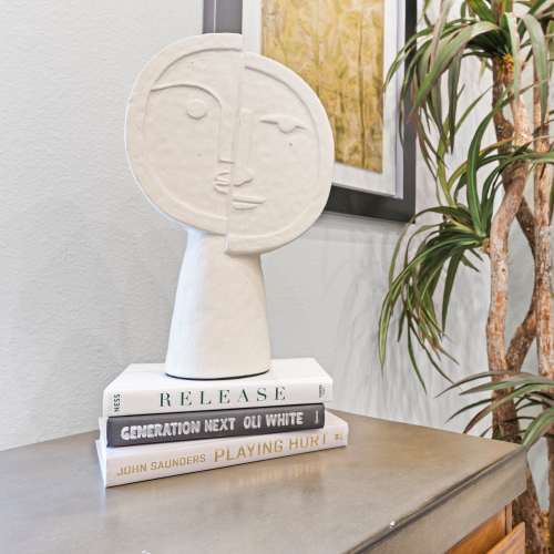 A close-up shows an abstract face sculpture resting on a stack of three books at The Ambrose in Houston, Texas, 