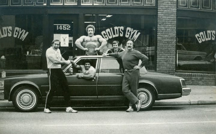 Vintage photograph of five body builders taken in front of Golds Gym. 