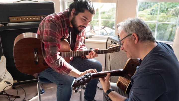 Young male instructor teaching older male student to play acoustic guitar | music schools around Jacksonville