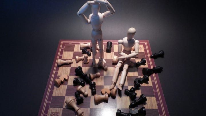 scattered chess board with two mannequins standing on top of it
