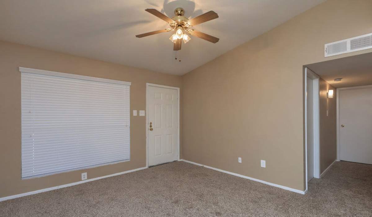 Empty living room with beige walls, carpeted floor, fireplace, ceiling fan, and two large windows at The Breakers in Texas City, Texas