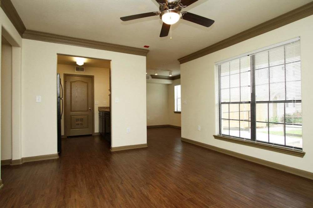 Open layout living area with wood-style flooring and ceiling fan, leading to kitchen and entrance at Villa Del Prado in Houston, Texas