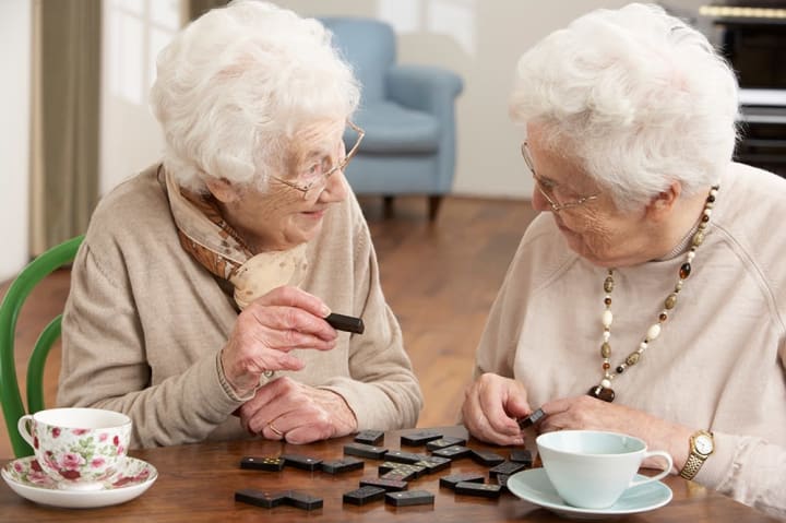 Two residents playing dominoes together at {{location_name}} in {{location_city}}, {{location_state_name}}