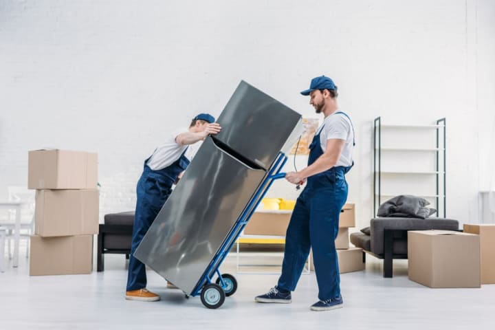 Two professional movers transporting a fridge on a dolly