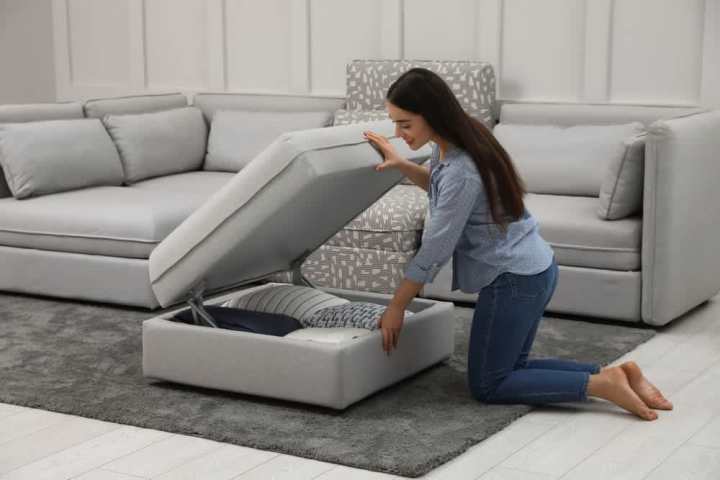 Young woman storing pillows and blankets in an ottoman with built-in hidden storage