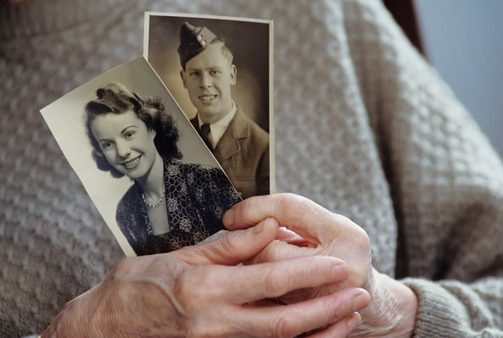 Female senior holding two old black and white photographs of a young man and young woman.