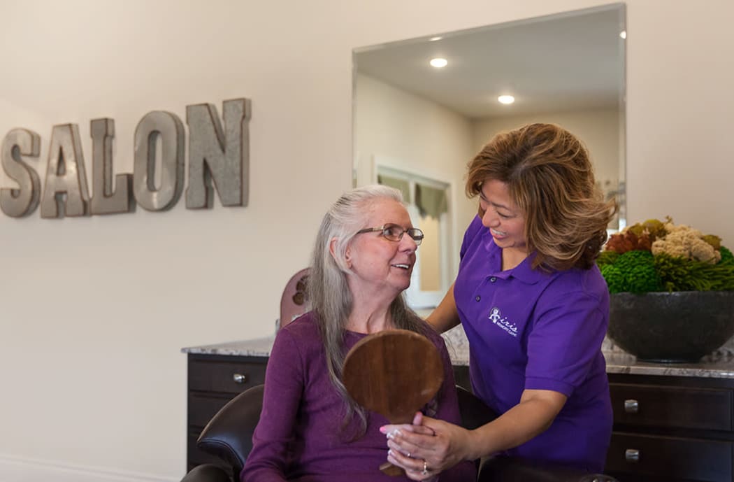 Staff member assisting senior with mirror at Iris Memory Care of NW Oklahoma City in Oklahoma City, Oklahoma.