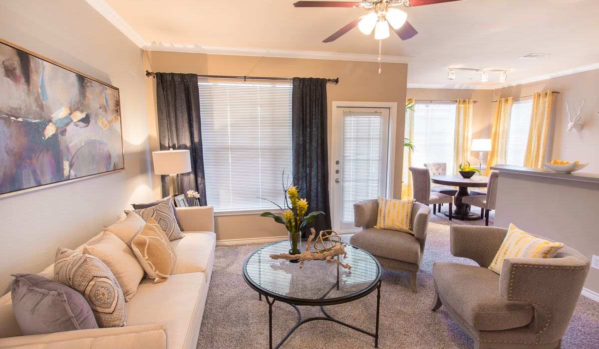 Living room with plush carpeting, couch, coffee table, ceiling fan, large windows and access to patio through door at Cobblestone Park in Manvel, Texas