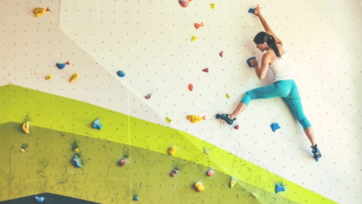 young woman climbing a white and green wall in a rock climbing gym | rock climbing gyms near Peoria