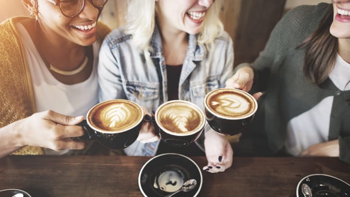 Three smiling women holding latte cups together | coffee shops near The Woodlands