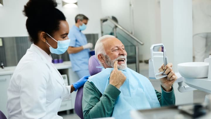A man looking at his teeth in a mirror at a dentist office | dentists in Savannah