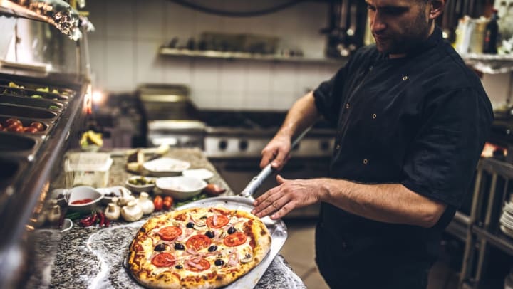 Chef placing a whole pizza on the counter in a restaurant kitchen | pizzerias in Keller