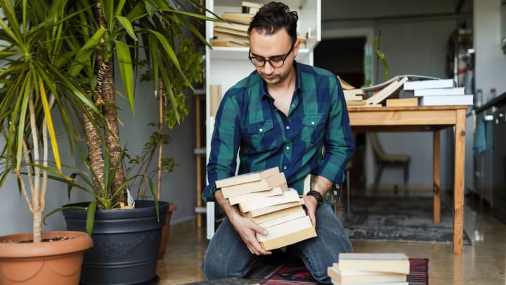 A man wearing glasses and a plaid shirt organizes a stack of books in his home