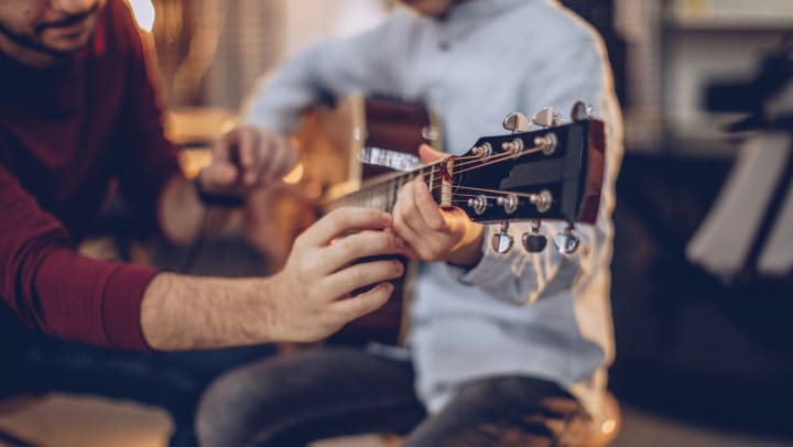 A man teaching a student a chord on a guitar