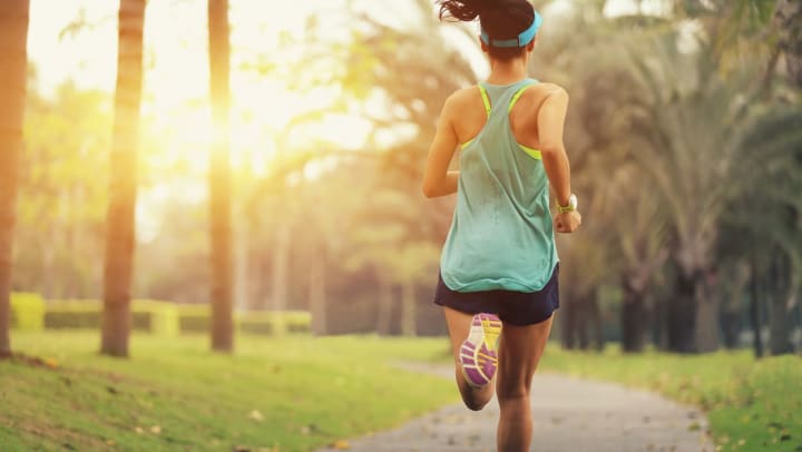 Woman running on a paved path surrounded by lots of green space and trees at a park