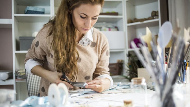 Woman cutting paper over a table with lots of craft supplies