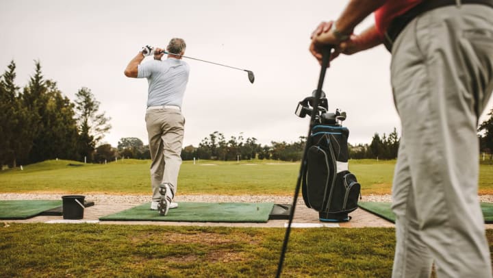 Man practicing his golf swing with a coach at a range